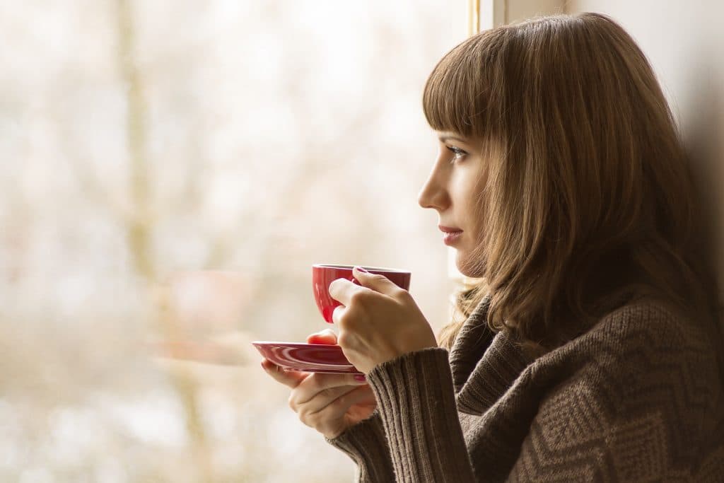 Piękna dziewczyna pije kawę lub herbatę w pobliżu okna